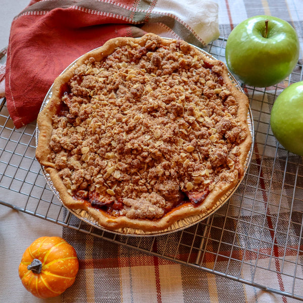 Apple pie on a cooling rack with apples and pumpkins on a checkered tablecloth
