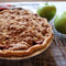 Apple pie with crumble topping on a cooling rack with green apples in the background.