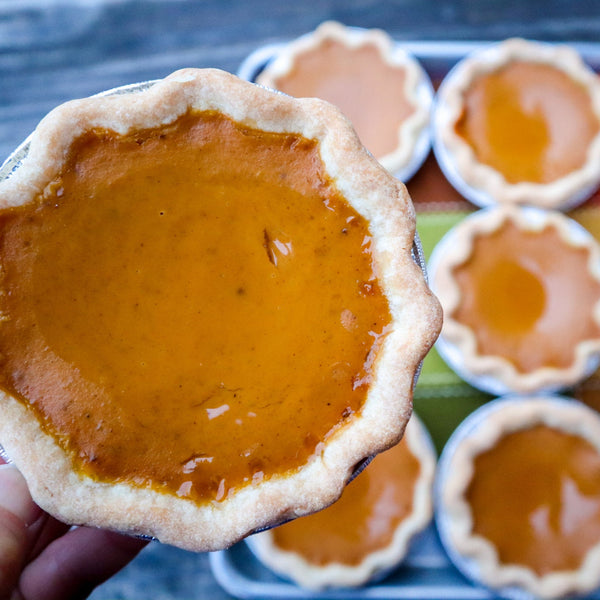 Pumpkin pie held by a hand with more pies in the background