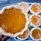 Pumpkin pie held by a hand with more pies in the background