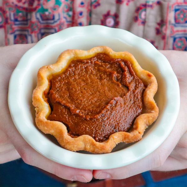 Pumpkin pie held in a white dish with a patterned fabric background