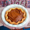 Pumpkin pie held in a white dish with a patterned fabric background